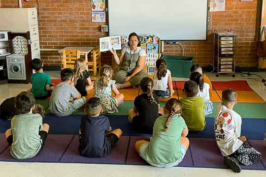 Teacher leads a circle of students reading a book.