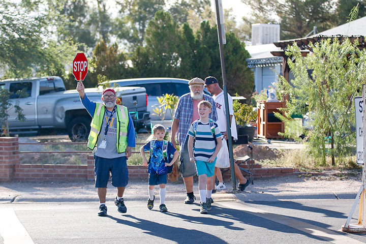 A crossing guard leads two boys and their parents across the street