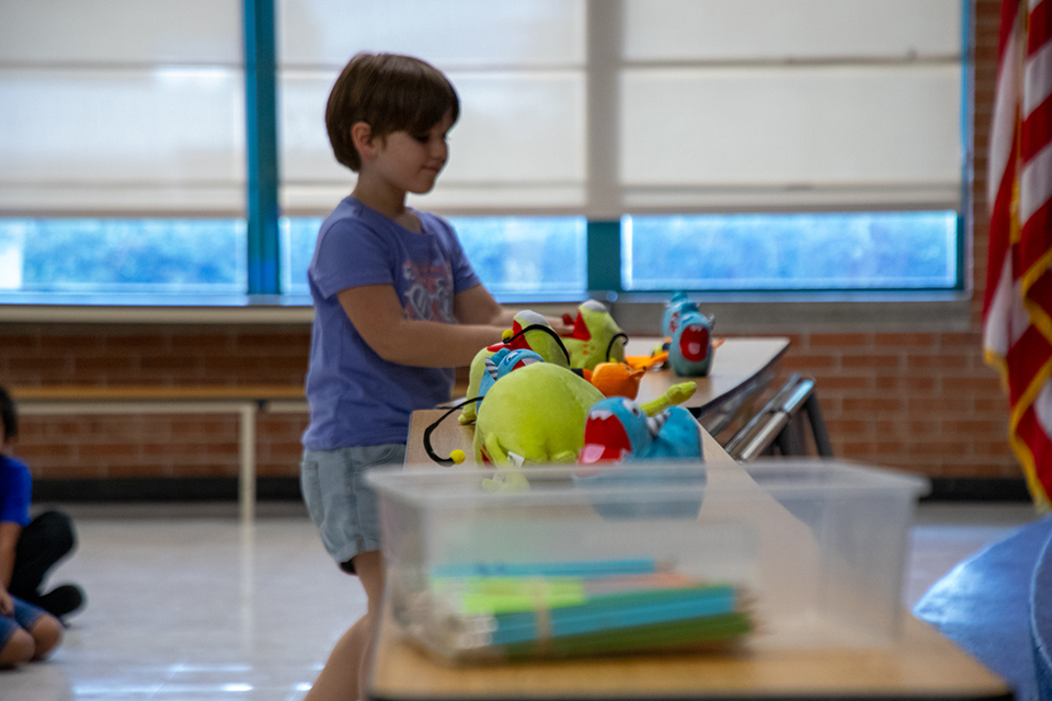 A girl in a purple shirt picks out a toy from the table