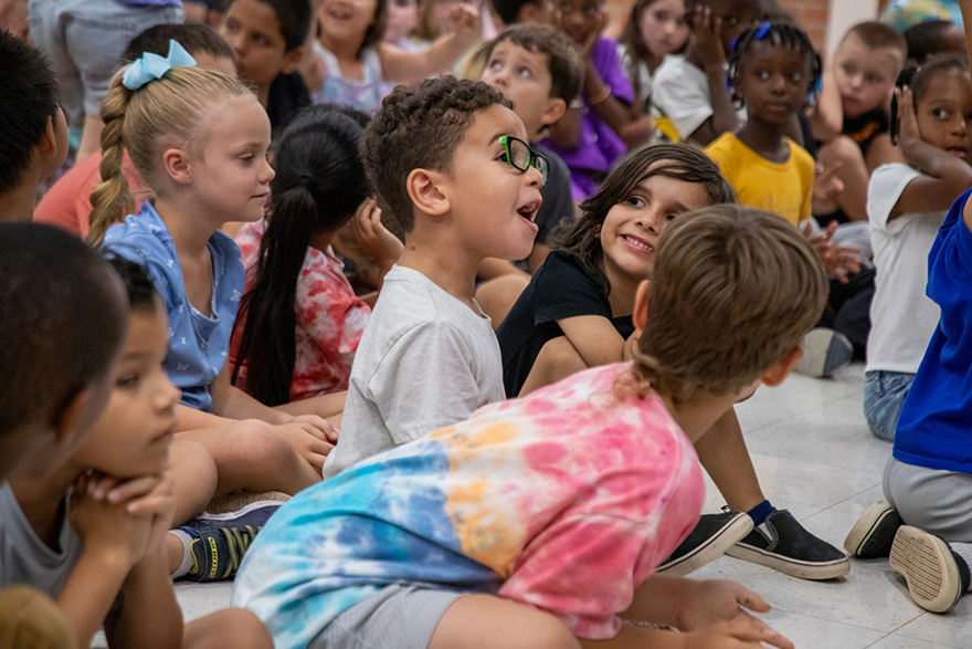 A boy in glasses laughs during the assembly, with other students smiling around him