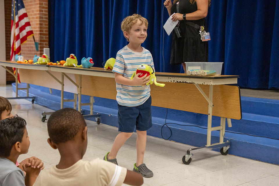 A little boy in a striped shirt holds his stuffed toy prize